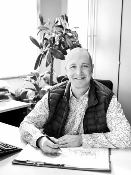 Profilbild Johannes Eichinger vor dem Computer mit einem Plan am Schreibtisch